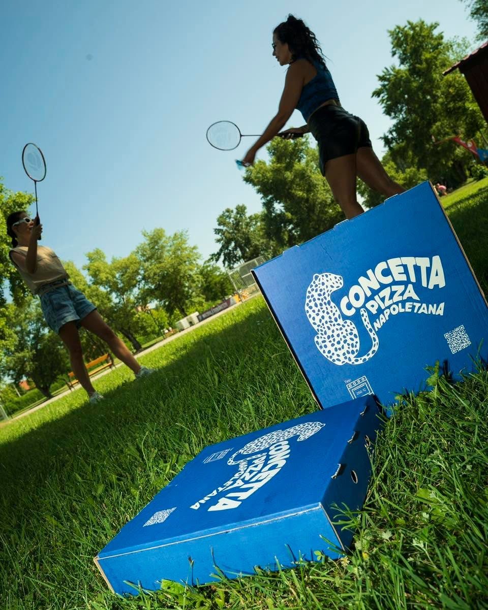 Elviteles Concetta pizzásdobozok a fűben Dunakeszin, a háttérben tollasozó barátnők